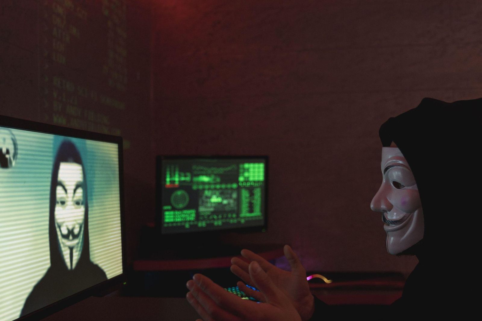 Person wearing an anonymous mask in front of computer screens during a video call